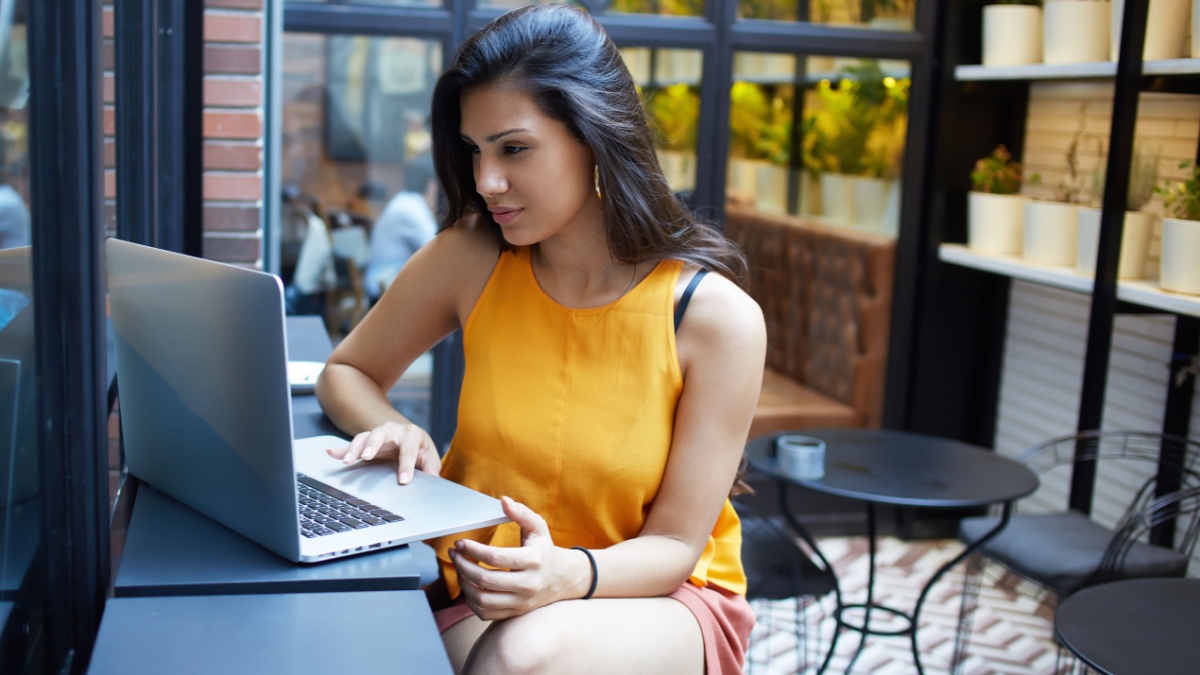 Gorgeous young woman sitting with open laptop computer in modern coffee shop interior, female freelancer using net-book for her distance wor.