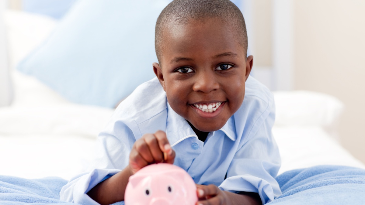 Young boy smiling at the camera while putting money into his piggy bank.