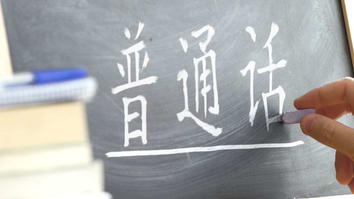 Hand writing on a blackboard in a language class with the text