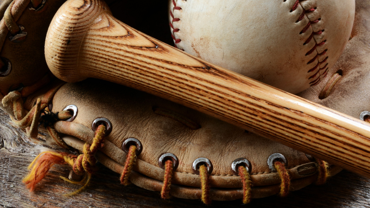 A close up image of an old used baseball, baseball bat, and baseball glove.