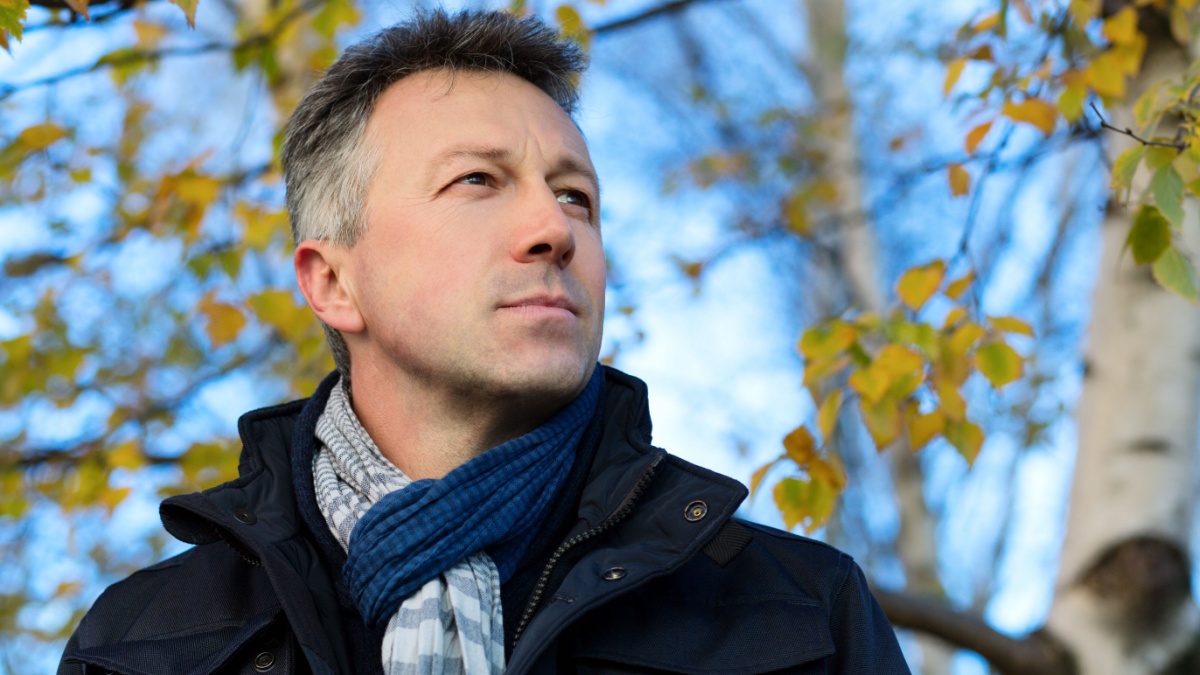 Handsome happy smiling man. Outdoor autumn male portrait. Attractive confident middle-aged man posing in city park, birch grove.