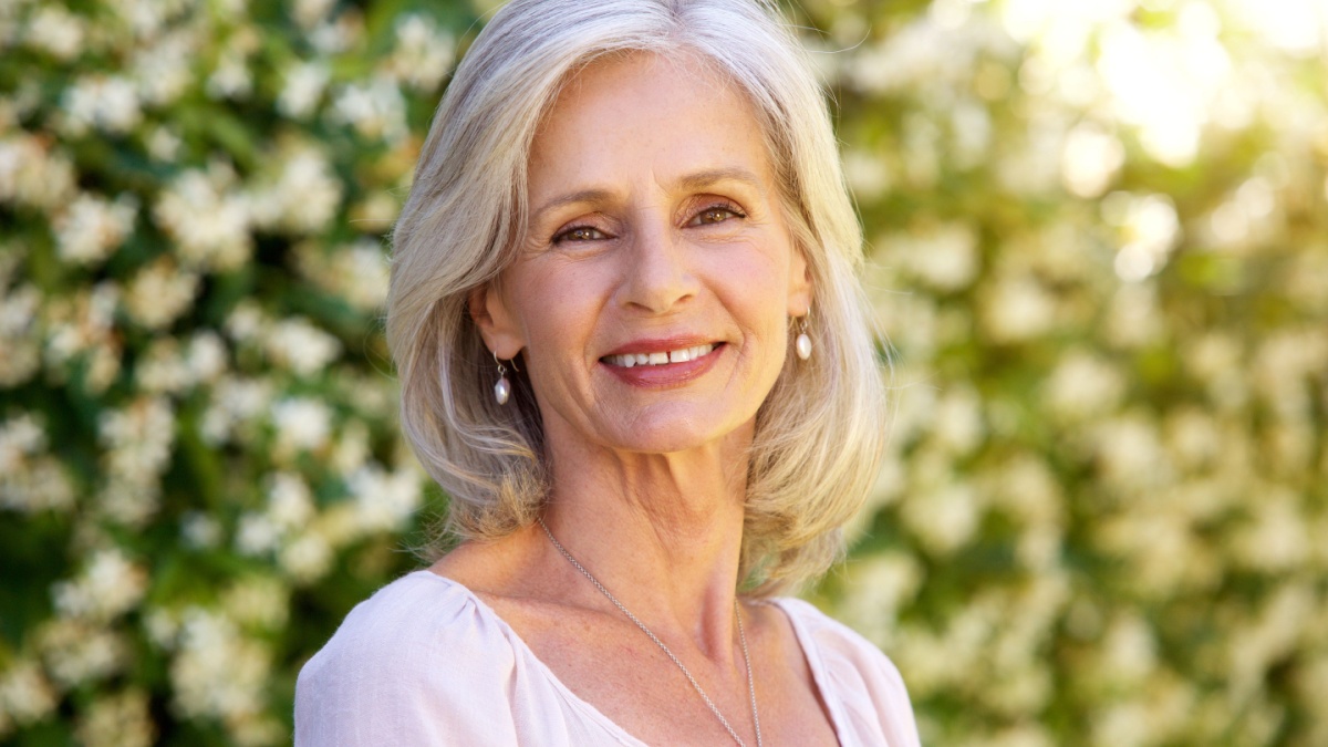Close up portrait of happy older woman standing outside in summer.