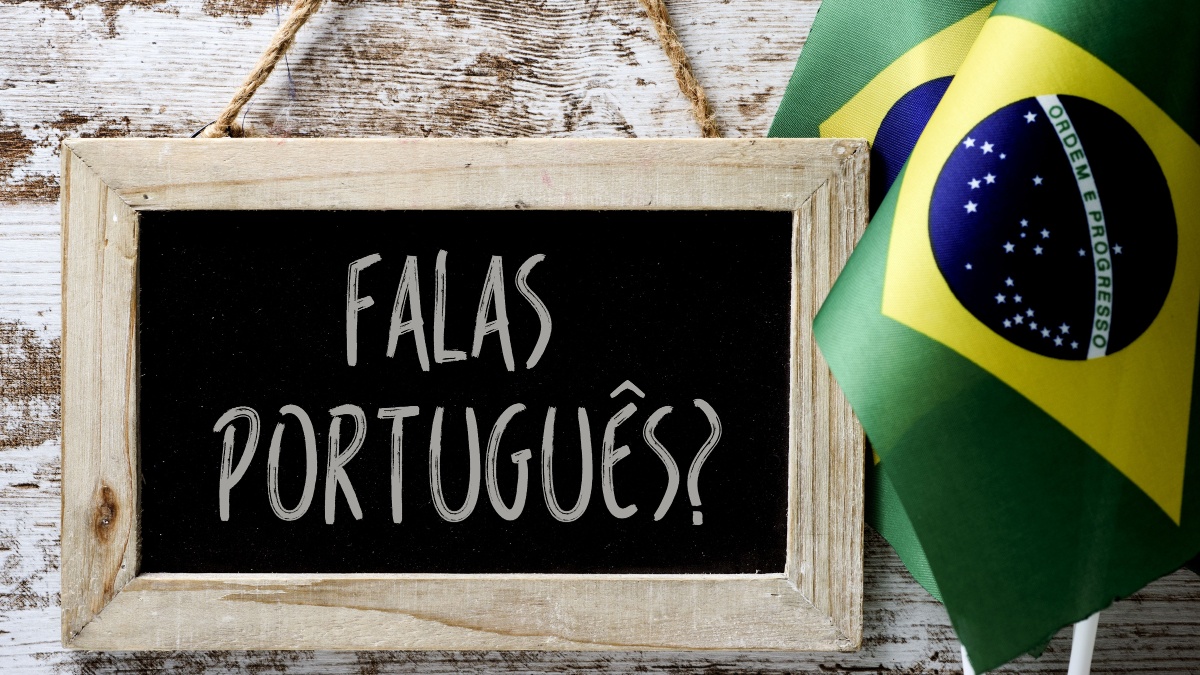 a wooden-framed chalkboard with the question falas portuges? do you speak Portuguese? written in Portugese, and some flags of Brazil against a rustic wooden background