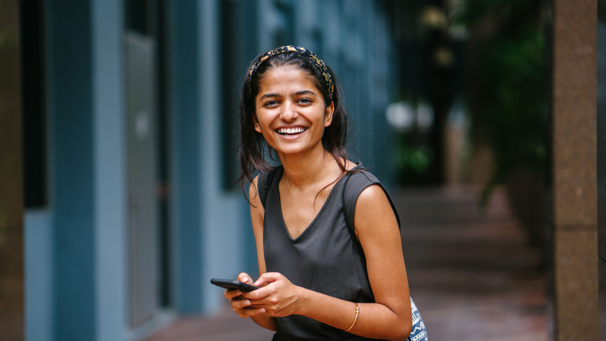 Portrait of young and attractive Indian Asian woman standing in the sun against a dark background in the city.