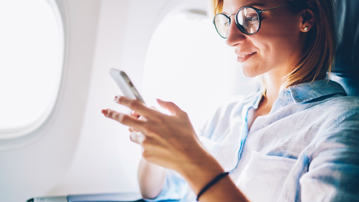 Attractive female passenger of airplane read news from networks via smartphone and wifi on board, young woman sending message on phone traveling by plane in first class connecting to wireless on phone.