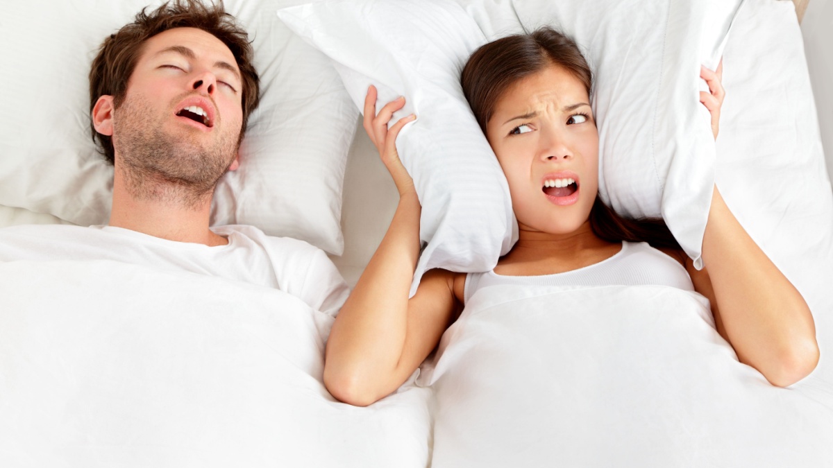 Snoring man. Couple in bed, man snoring and woman can not sleep, covering ears with pillow for snore noise. Young interracial couple, Asian woman, Caucasian man sleeping in bed at home.