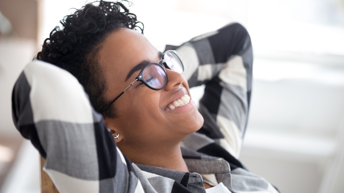 Close up relaxed glad african businesswoman holding hands behind head with closed eyes smiling in office at workplace.