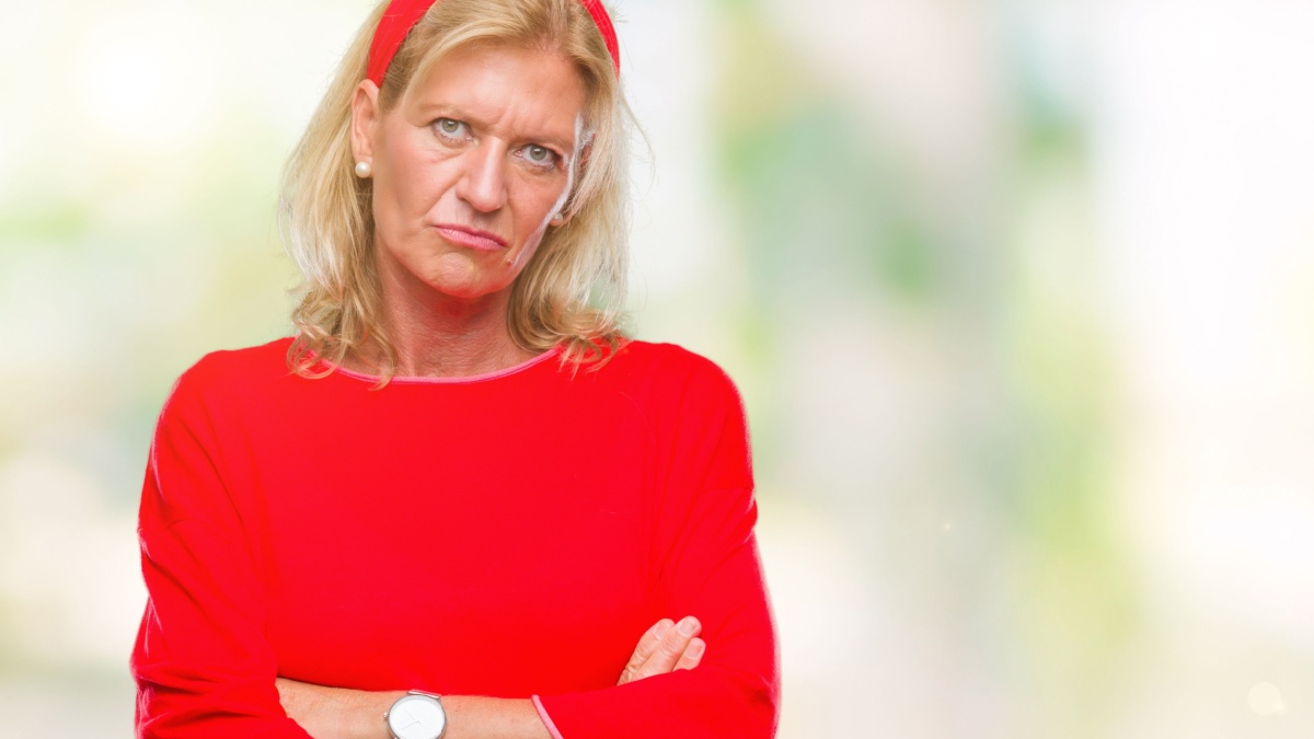 Middle age blonde woman over isolated background skeptic and nervous, disapproving expression on face with crossed arms. Negative person.