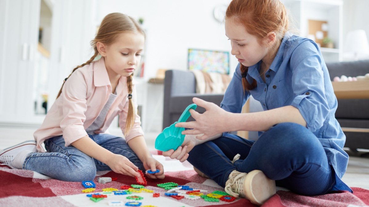 Full length portrait of two sisters playing with puzzles sitting on floor