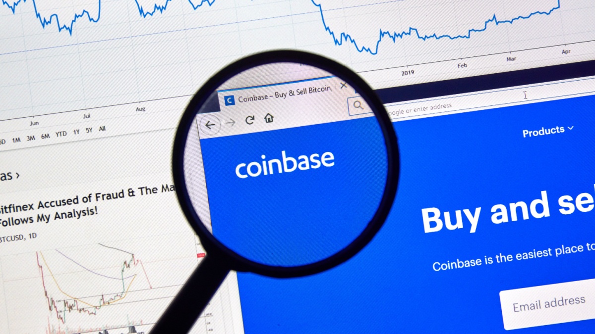 Coinbase cryptocurrency digital assets exchange logo and home page on a laptop screen under magnifying glass.