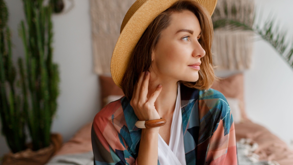 Close up portrait of beautiful romantic woman in straw hat chilling over bohemian interior wood accessories.
