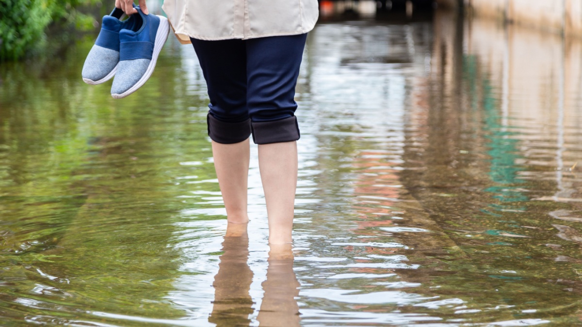 Woman walking on flooding road with holding shoes after the heavy rains,
