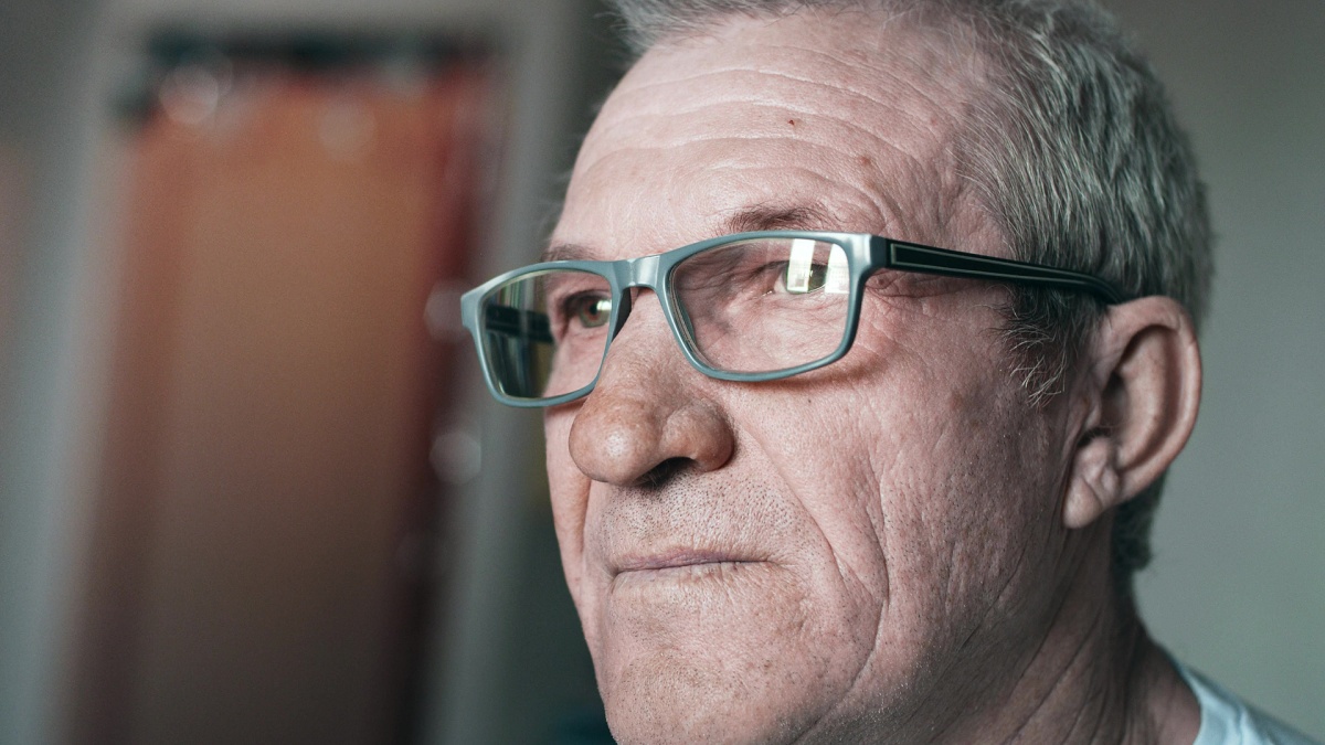 Close-up portrait of an elderly man with glasses, looking away.