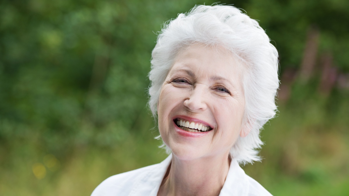 Vivacious laughing grey haired senior woman outdoors in a lush green park, close up portrait.