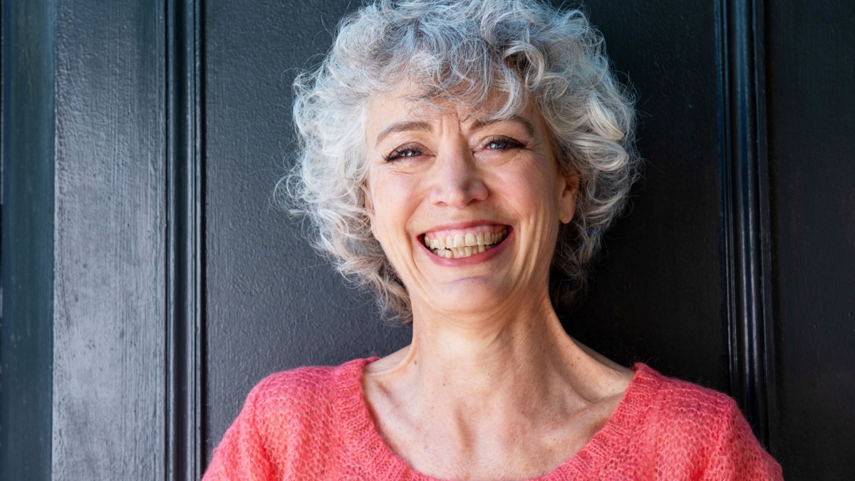 Close up front portrait of happy middle aged woman with gray curly hair.