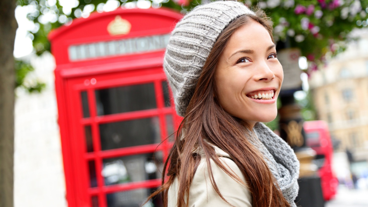 London people - woman by red phone booth. Portrait of beautiful smiling happy young female casual professional business woman walking outside in City of Westminster, London, England, Great Britain.