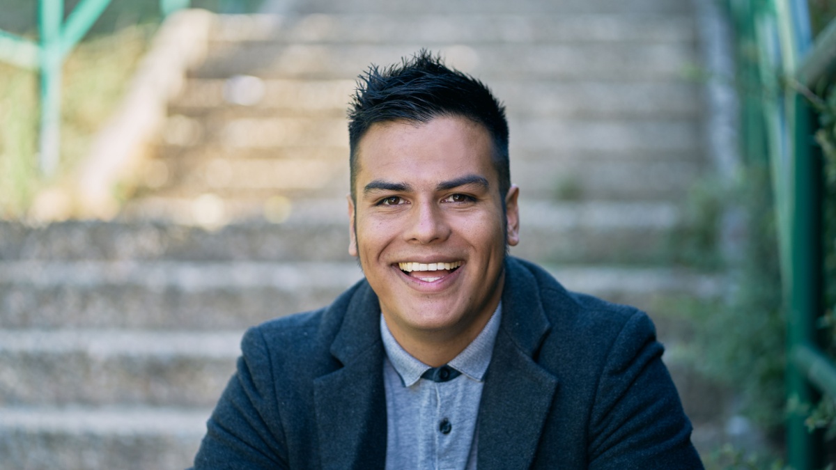 portrait of a handsome Hispanic boy sitting on the stairs putting on good pants and urban style clothing: jeans, blue shirt and dark jacket.