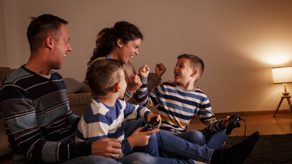 Parents with they children sitting at home on pleasant evening and playing games on console.They challenge each other to win .