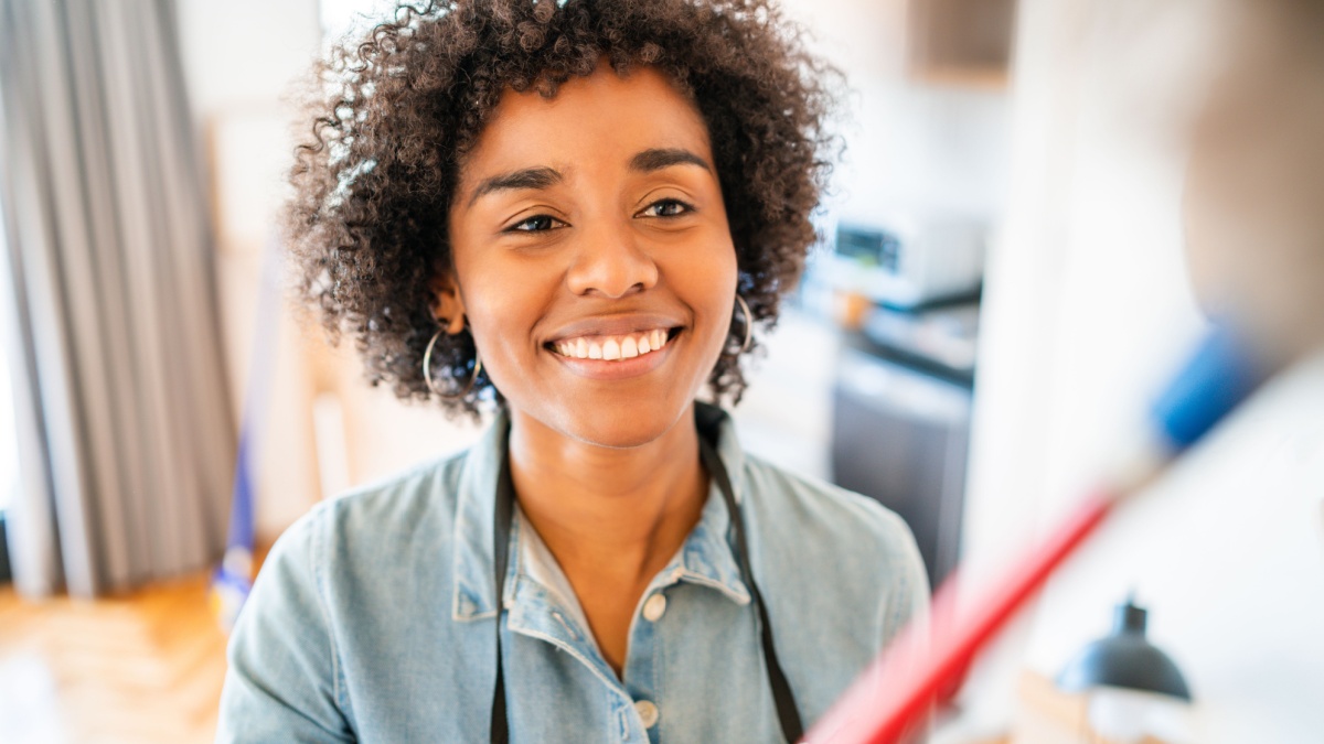 Portrait of young afro woman cleaning her new house with a duster. Housekeeping and cleaning concept.