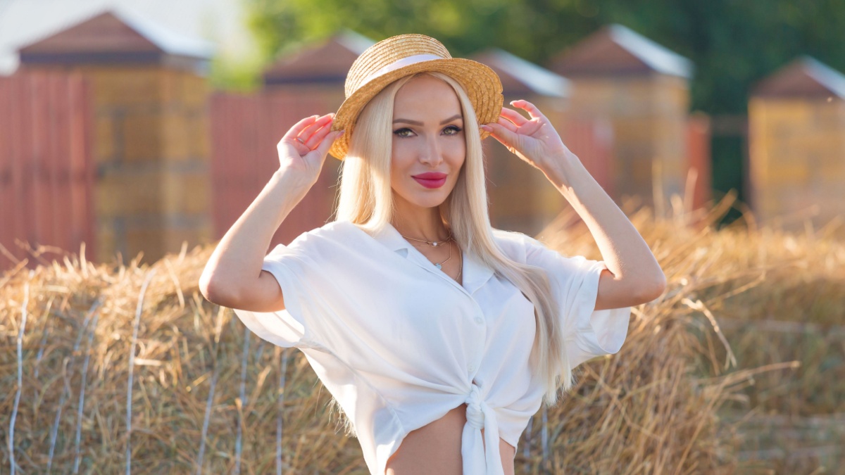 Beautiful blonde cow girl, wearing a white shirt and hat, has long hair.