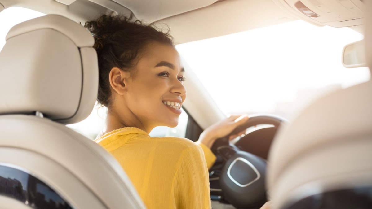 Own Car. Cheerful Black Woman Driving Auto Sitting In Driver's Seat In Automobile. Back View, Selective Focus.