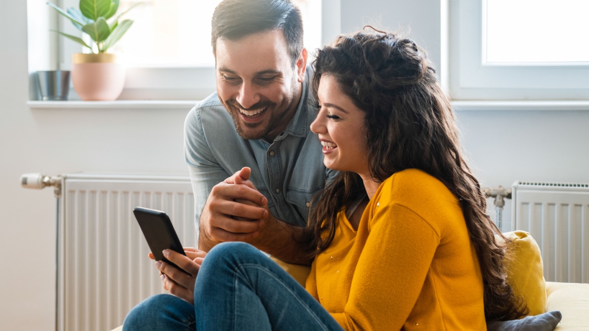 Cheerful couple using mobile phone at home stock photo.