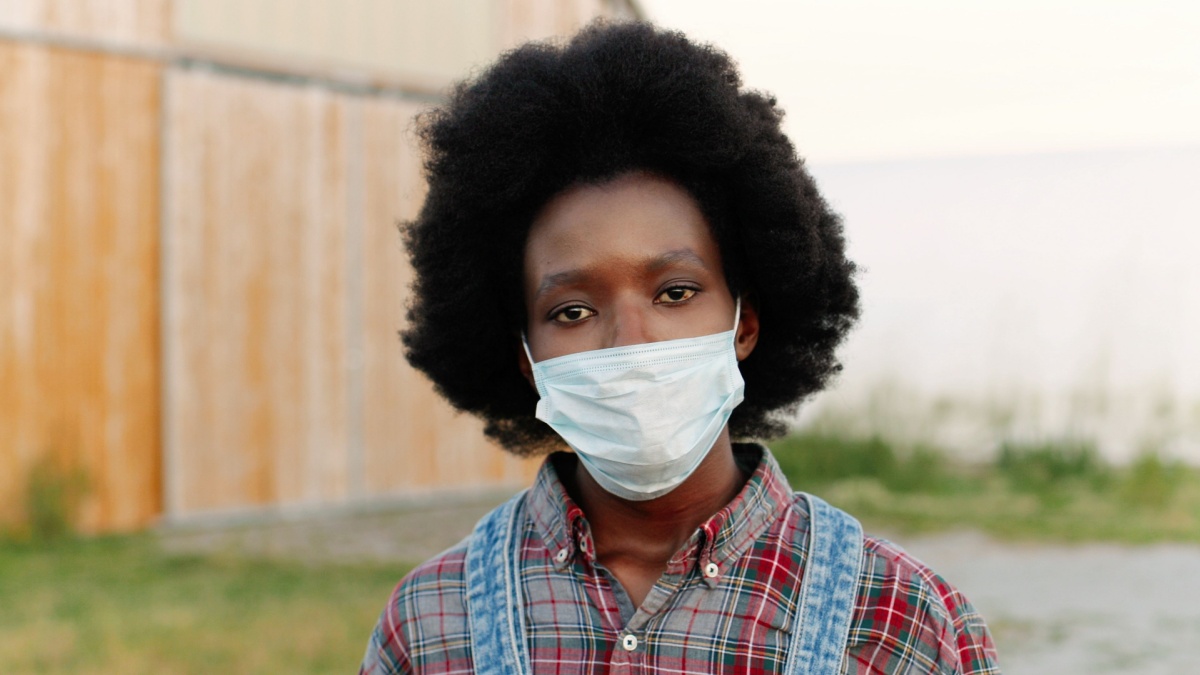 Close up of young African American sad woman with curly hair and in motley shirt outdoors looking at camera.