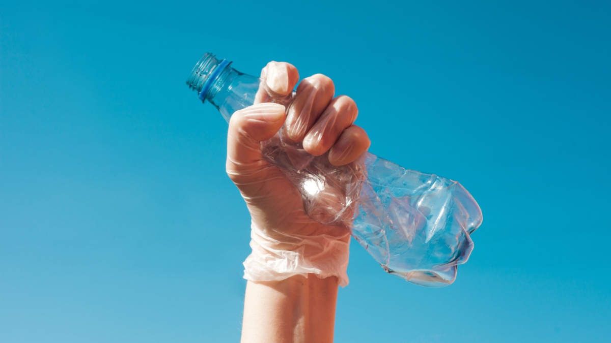 We are against plastic garbage. A hand in protective gloves clutches an empty disposable bottle. Separation of waste, recycling of plastics, the concept on a sky background.