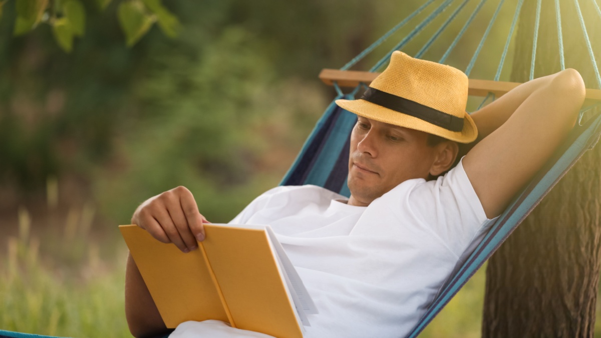 Man reading book in comfortable hammock at green garden.
