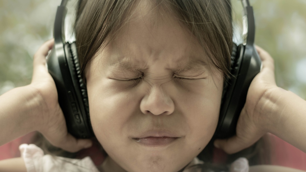 A little kid afraid of loud noise, sensitive to sound, covering ears.