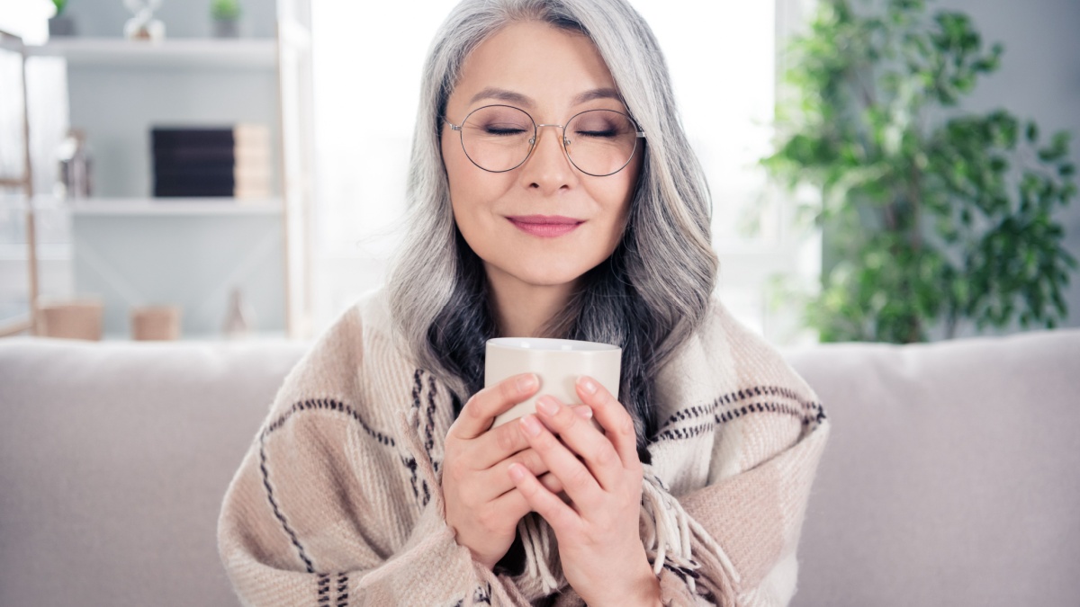 Photo portrait of senior woman dreamy smiling drinking hot tea sitting under plaid blanket at home.