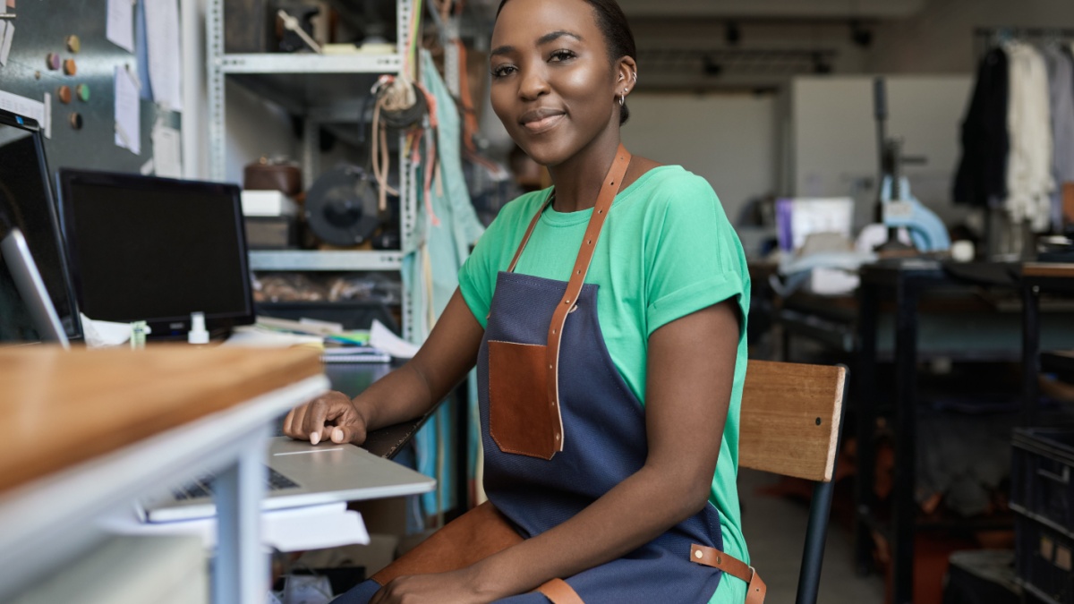 Smiling African female artisan using a laptop in her workshop.