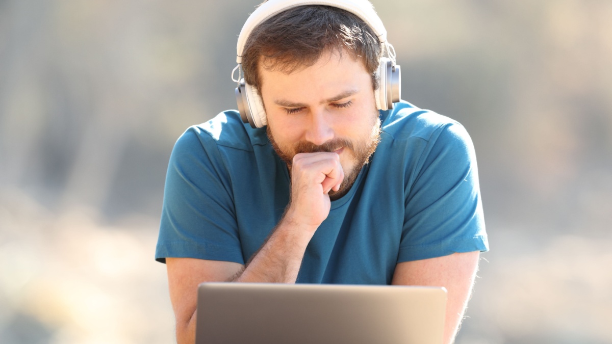 20 Legit Ways To Earn Money Online 11 Front view portrait of a man wearing wireless headphones listening and watching videos on laptop outdoors.