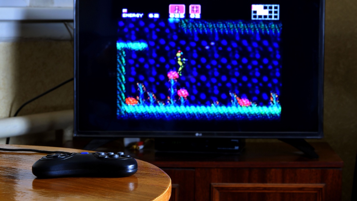 Sega mega drive video game controller on table with Super Metroid game on big display
