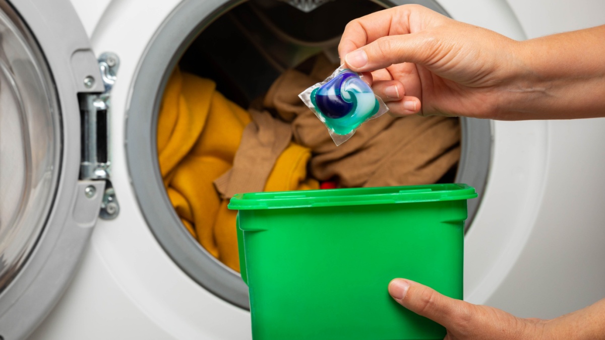 Woman putting laundry detergent capsule into washing machine indoors, closeup.Colorful laundry eco gel in capsule. Washing clothes.The concept of washing and cleanliness