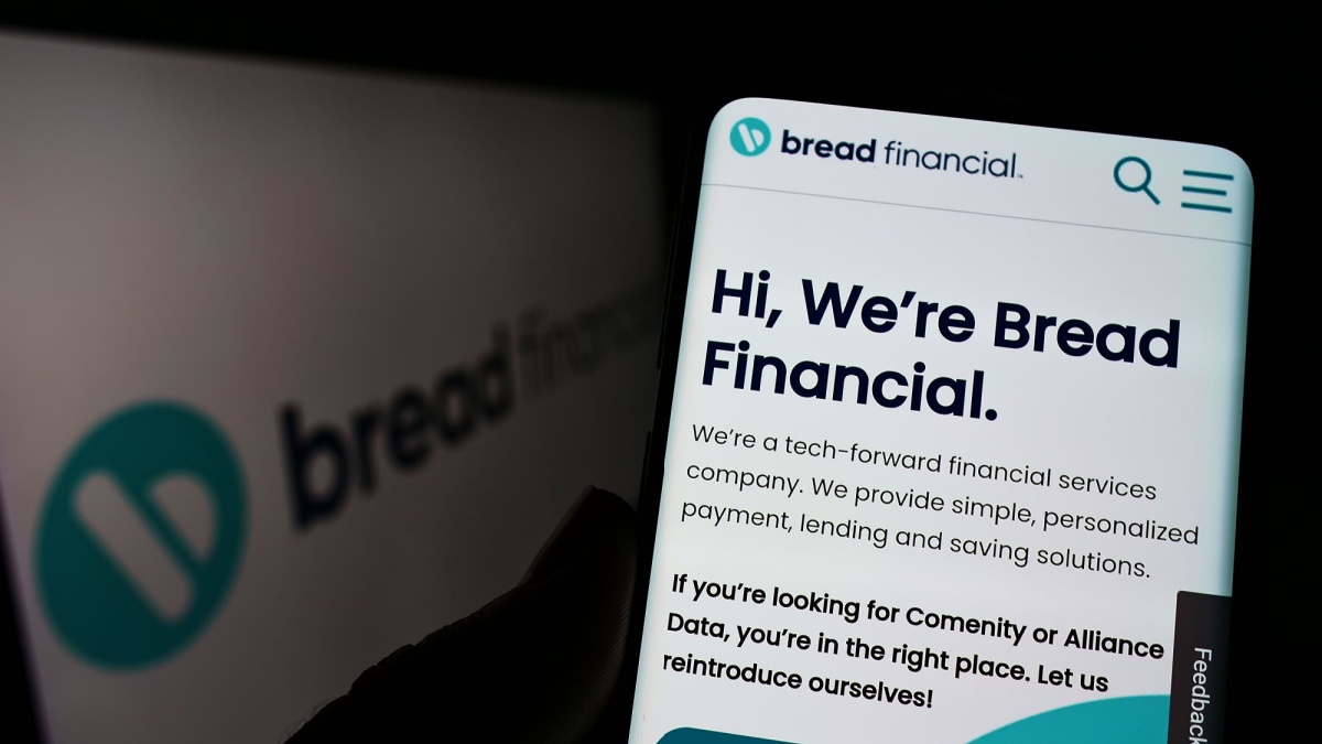 Person holding cellphone with webpage of US company Bread Financial Holdings Inc. on screen in front of logo. Focus on center of phone display.