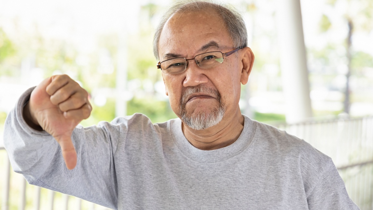 Unhappy and upset old senior man showing rejecting thumb down hand gesture.