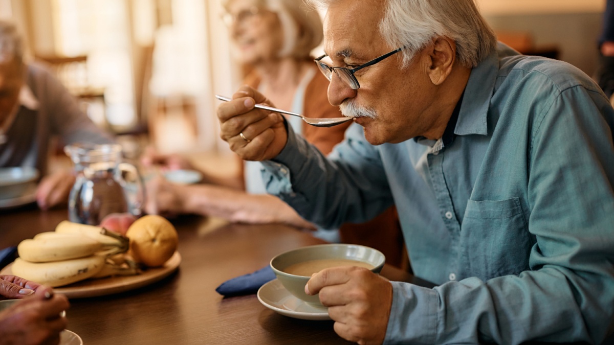 Mature man eating soup while having lunch at residential care home