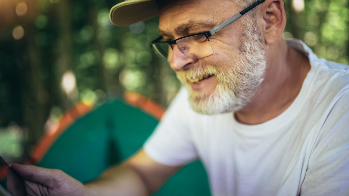 Mature man sitting in front of a tent and using digital tablet.