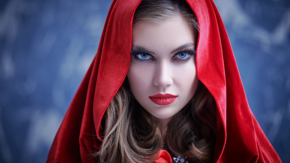 A bewitching young witch in a red cape with a hood looks with magnetic eyes at the camera. Magic tales. Halloween.
