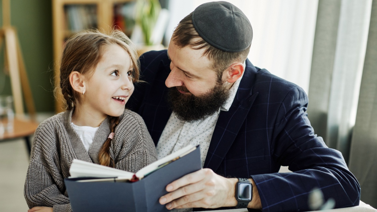 Portrait of smiling jewish father reading book with daughter at home