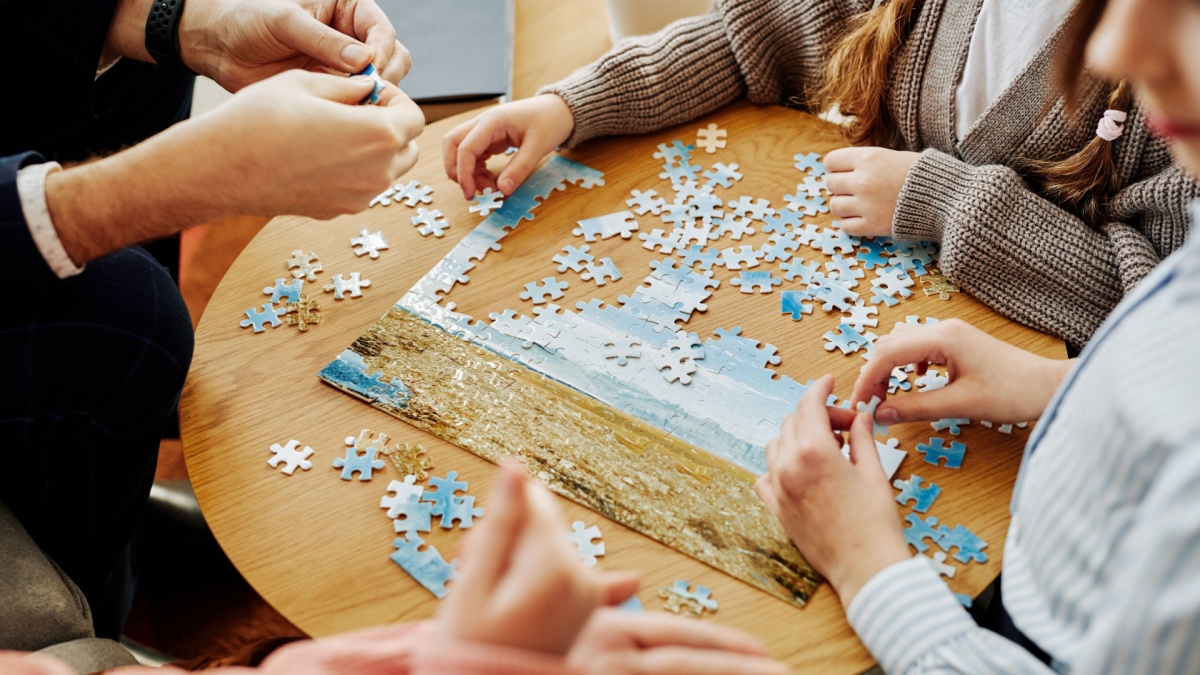 Close up of unrecognizable family playing jigsaw puzzle game together at home