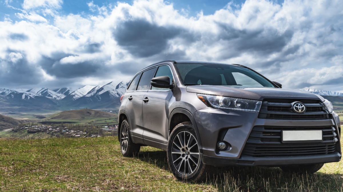 Toyota Highlander stands on a mountain slope against the backdrop of snow-capped mountains.