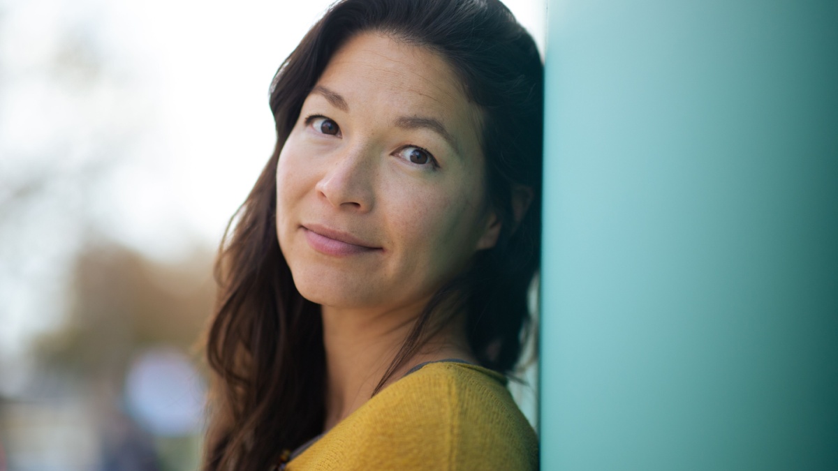 Close-up portrait of pretty young asian woman leaning to a wall outside and staring at camera.