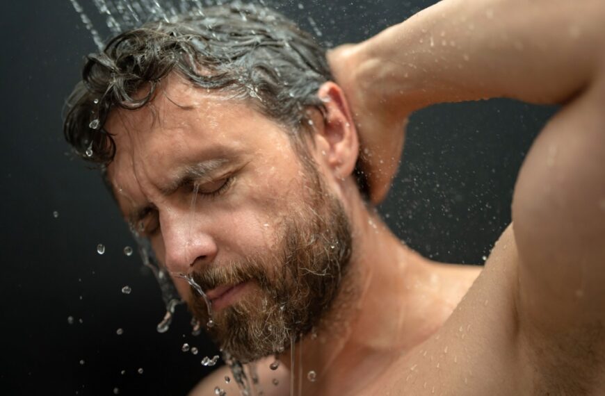 Millennial man washing hair in bath. Guy bathing shower head in bathtub.