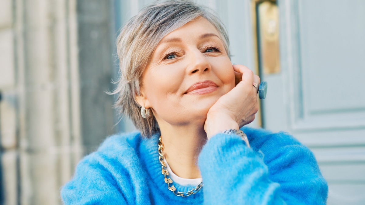 Outdoor portrait of beautiful 55 - 60 year old woman, wearing blue pullover.