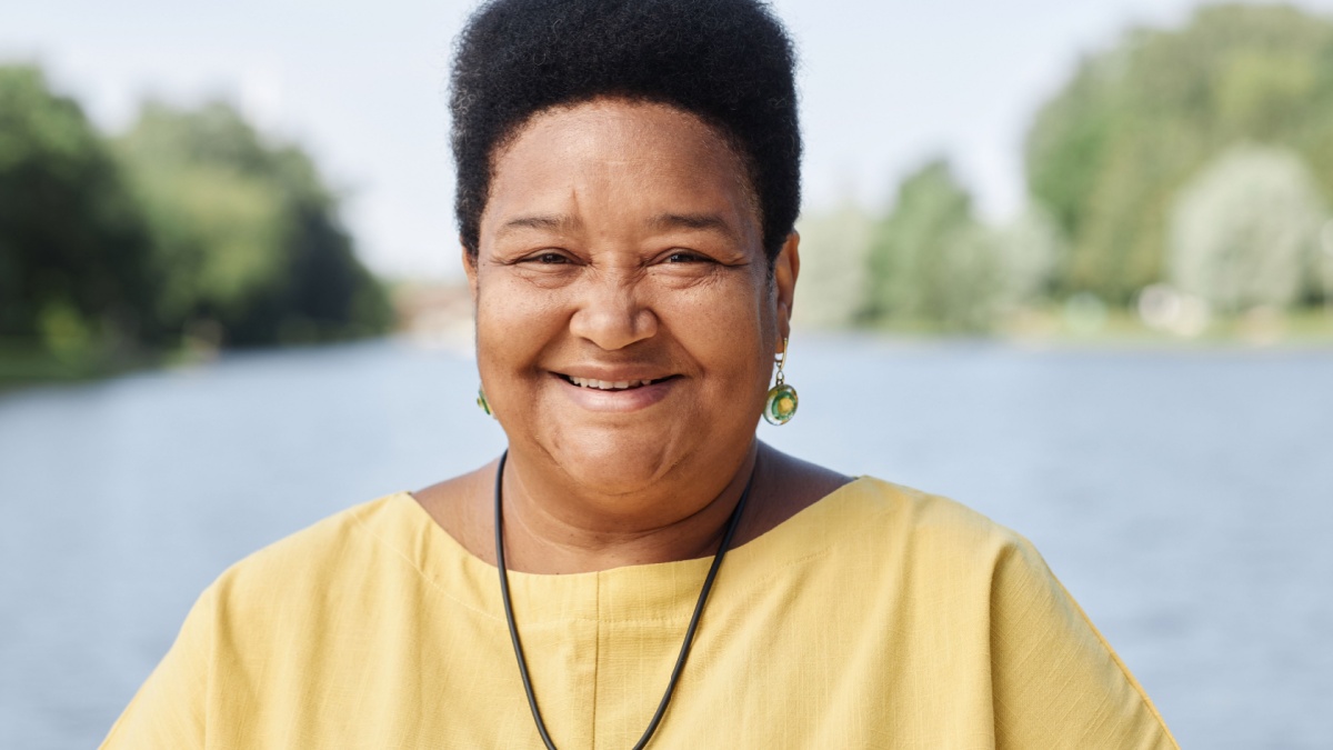 Candid front view portrait of senior Black woman smiling at camera outdoors.
