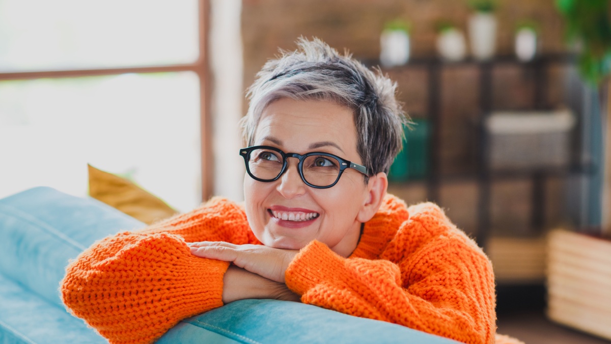 Portrait of lovely positive person sitting cozy sofa toothy smile daydreaming imagine apartment inside.