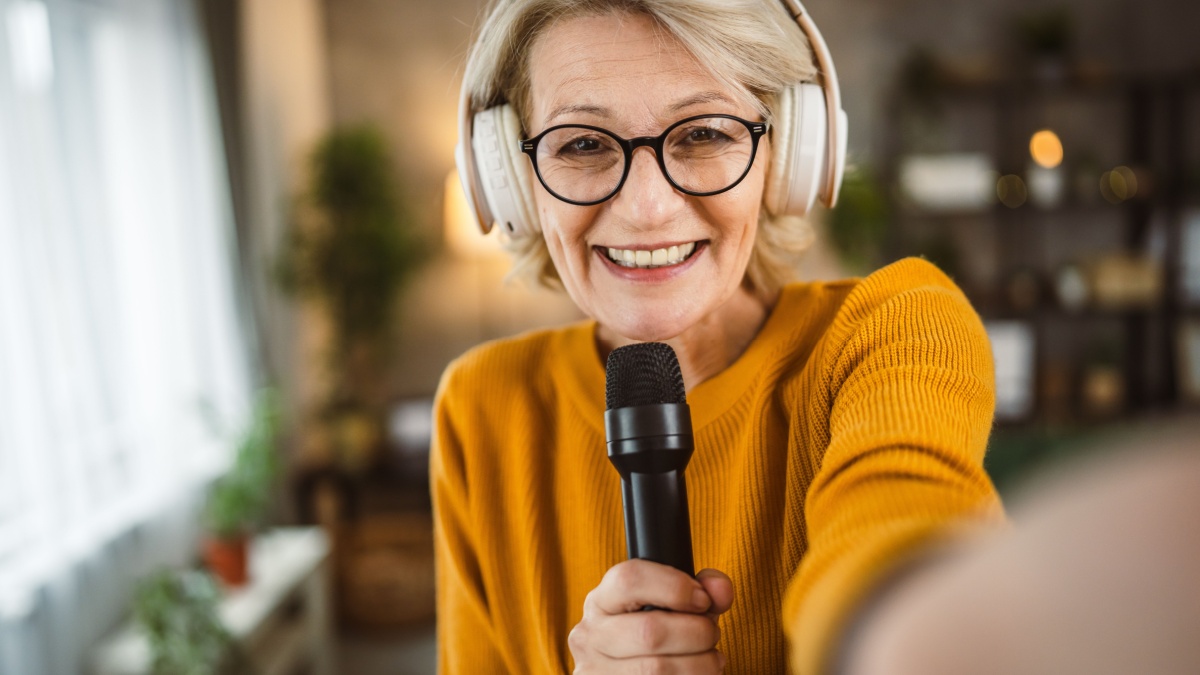 One woman mature blonde hold microphone at home happy smile sing dance.