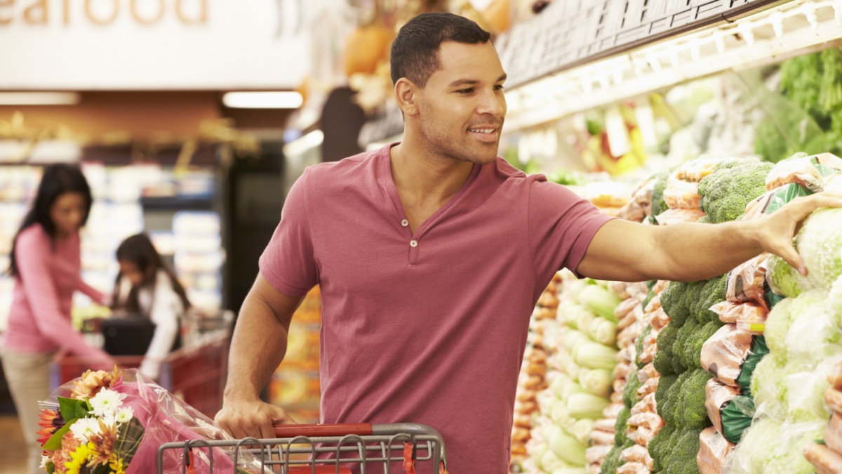 Man Pushing Trolley By Produce Counter In Supermarket.